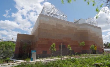 a large brick building against a blue sky with glasshouses on its roof